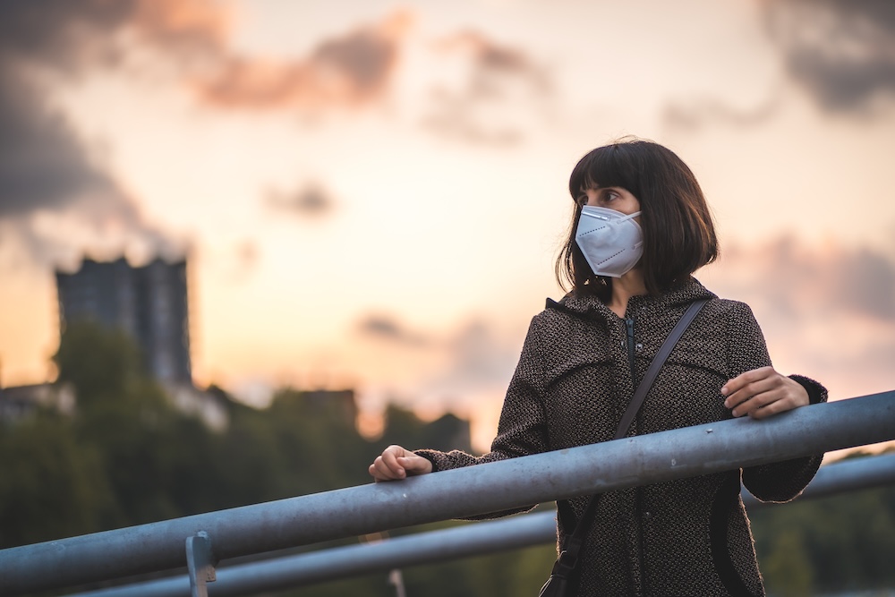 woman standing on a bridge with air pollution plant behind her