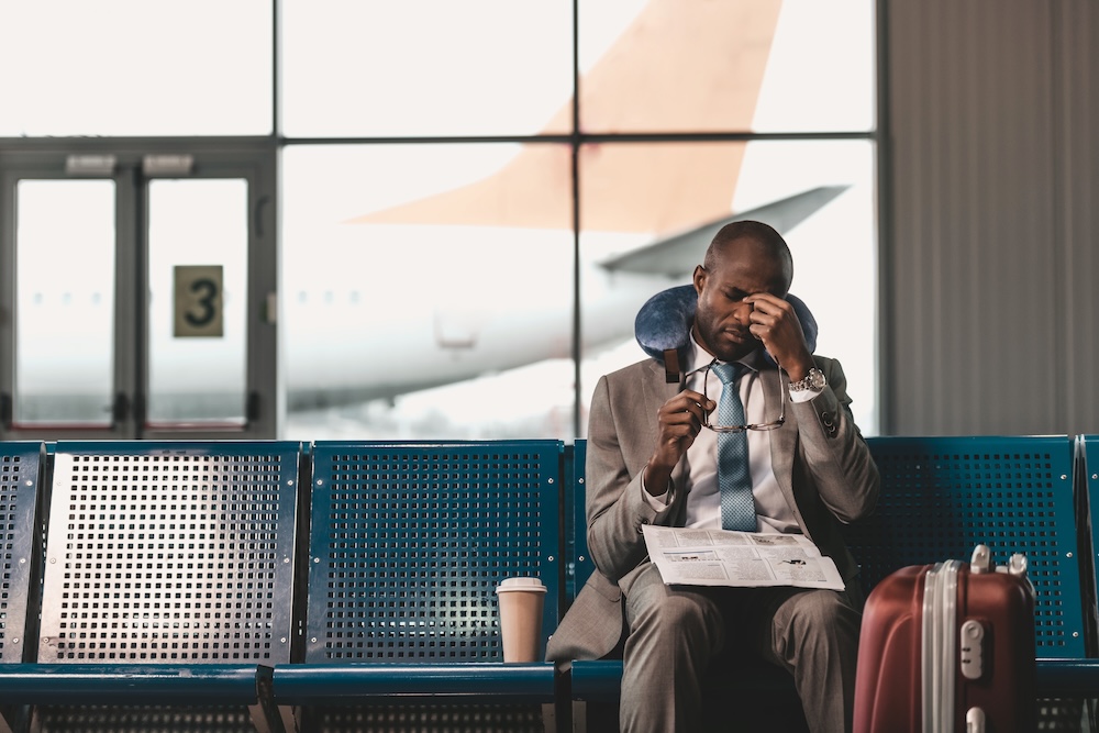 businessman waiting at the airport tired with a pillow around neck and newspaper