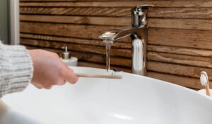 woman holding toothbrush under faucet