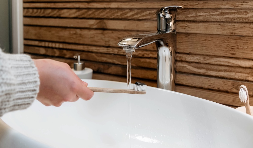 woman holding toothbrush under faucet