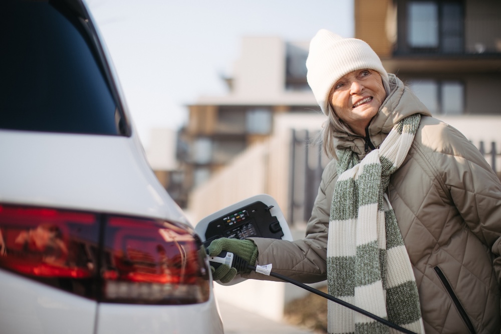 senior woman charging her electric vehicle in winter