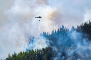 helicopter flying over wildfire dropping water