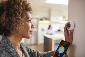 woman adjusting a smart thermostat with an smartphone app