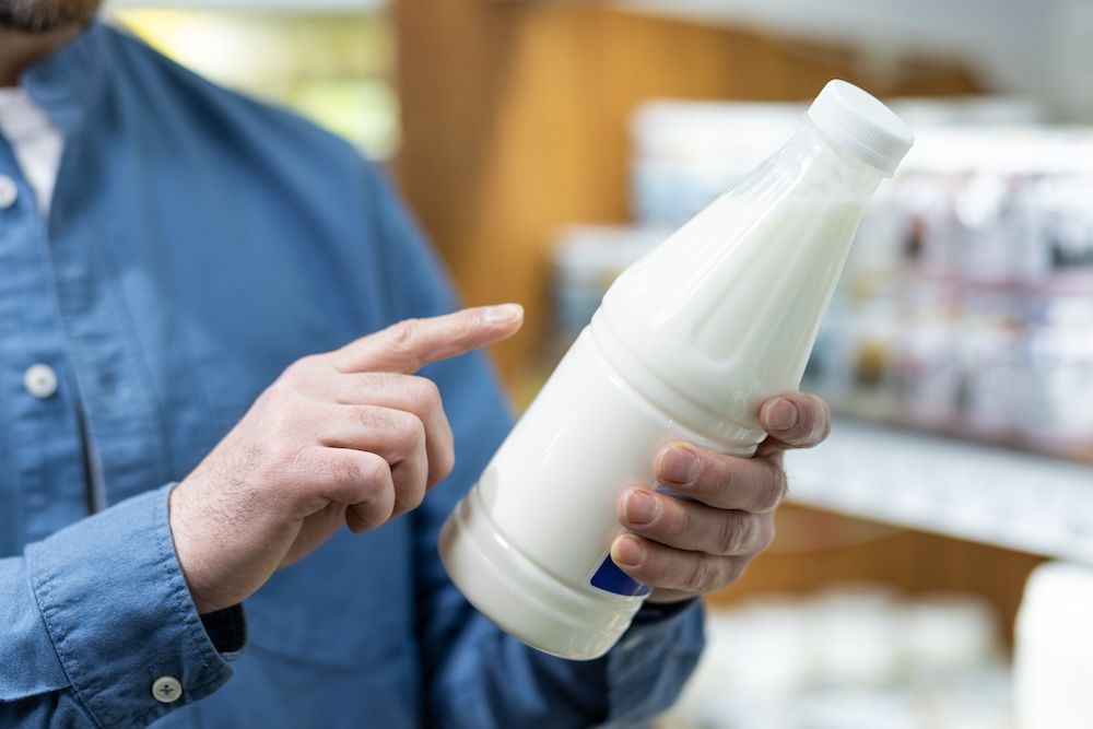 person looking at expiration date and ingredients on milk bottle