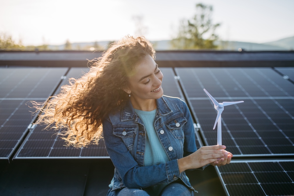 young woman holding wind turbine with solar panels behind her