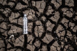 empty plastic water bottle laying on dry cracked drought impacted soil