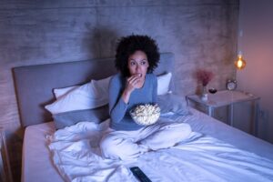 Woman in bed watching a movie and eating popcorn