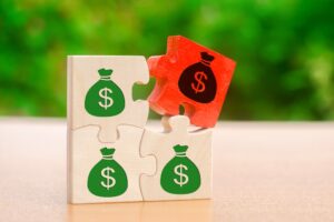 wooden puzzle pieces with green money bags and one red money bag