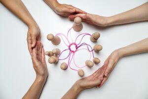 People holding hands around wooden figures tied together by thread
