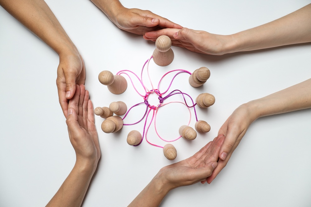 People holding hands around wooden figures tied together by thread