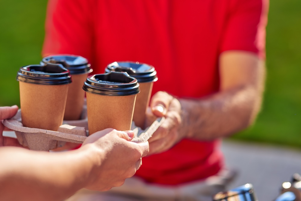 Person handing over carton of coffee cups