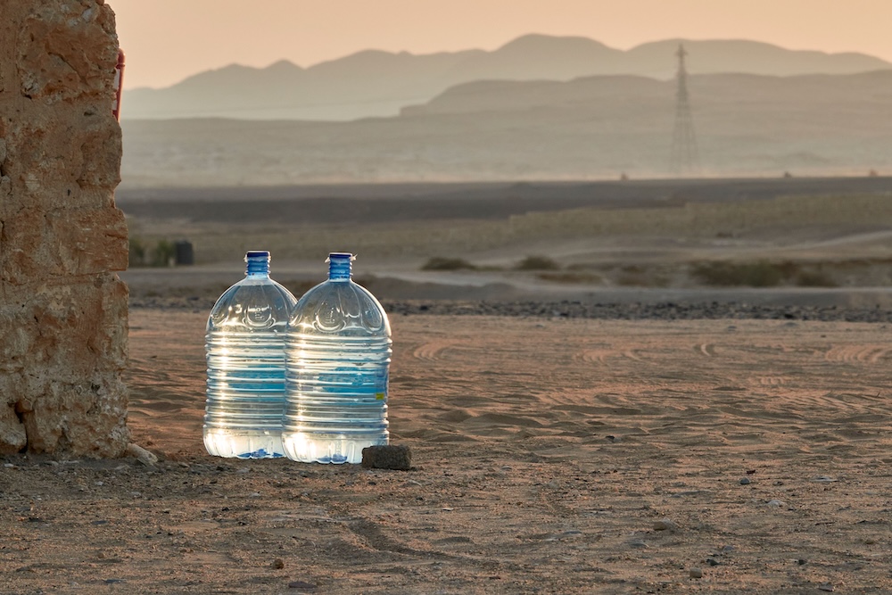 Two plastic containers of water sitting on dry land