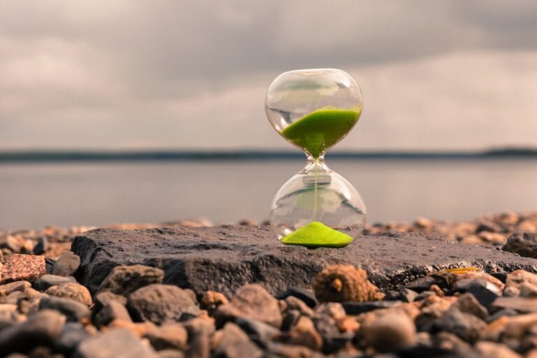 hourglass sitting near a lake with green sand pouring out
